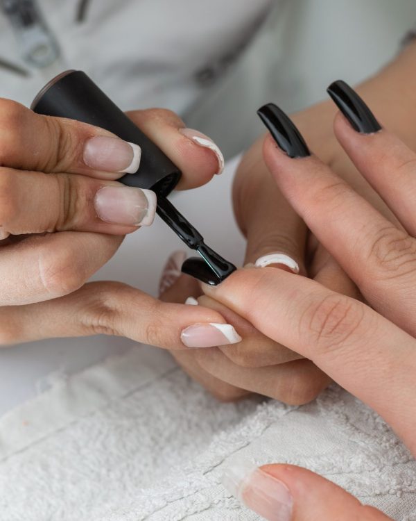 A closeup shot of a manicurist painting and designing nails of a female with a black nail polish